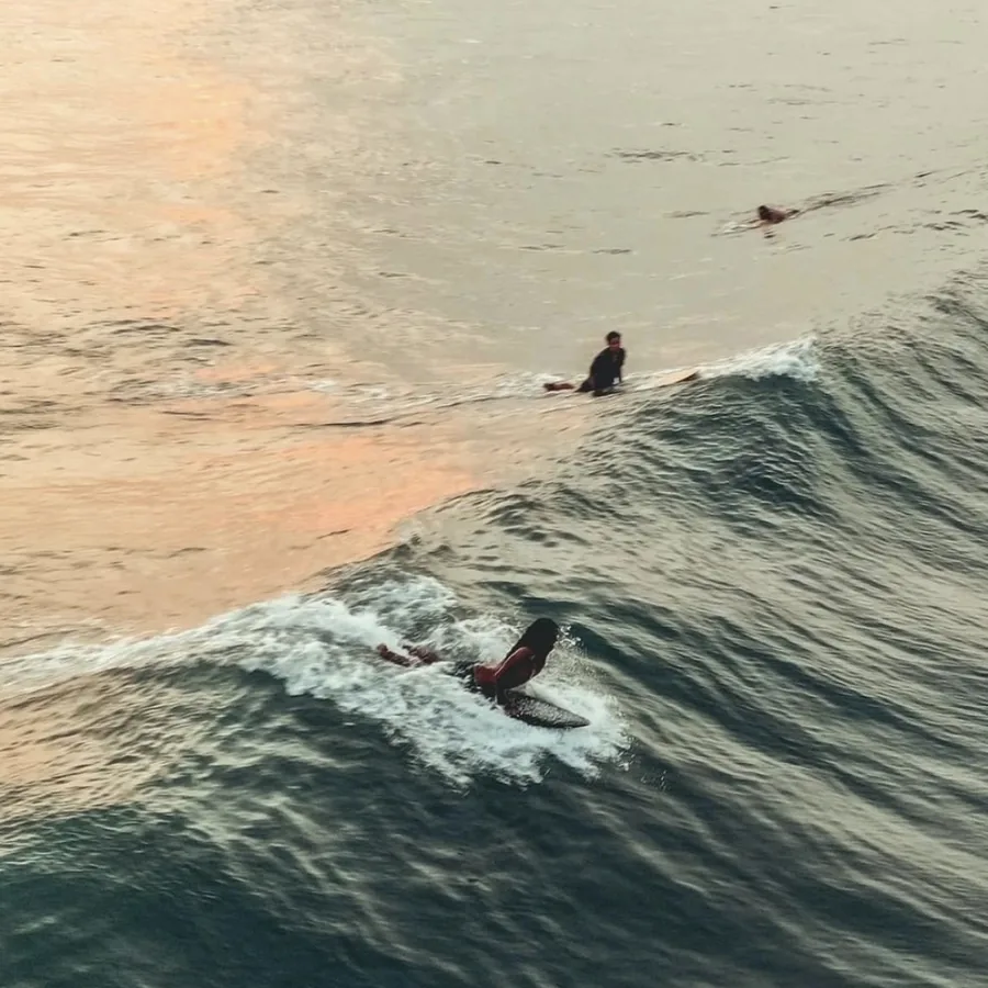 Surfers paddling into a wave at Uluwatu in the late light