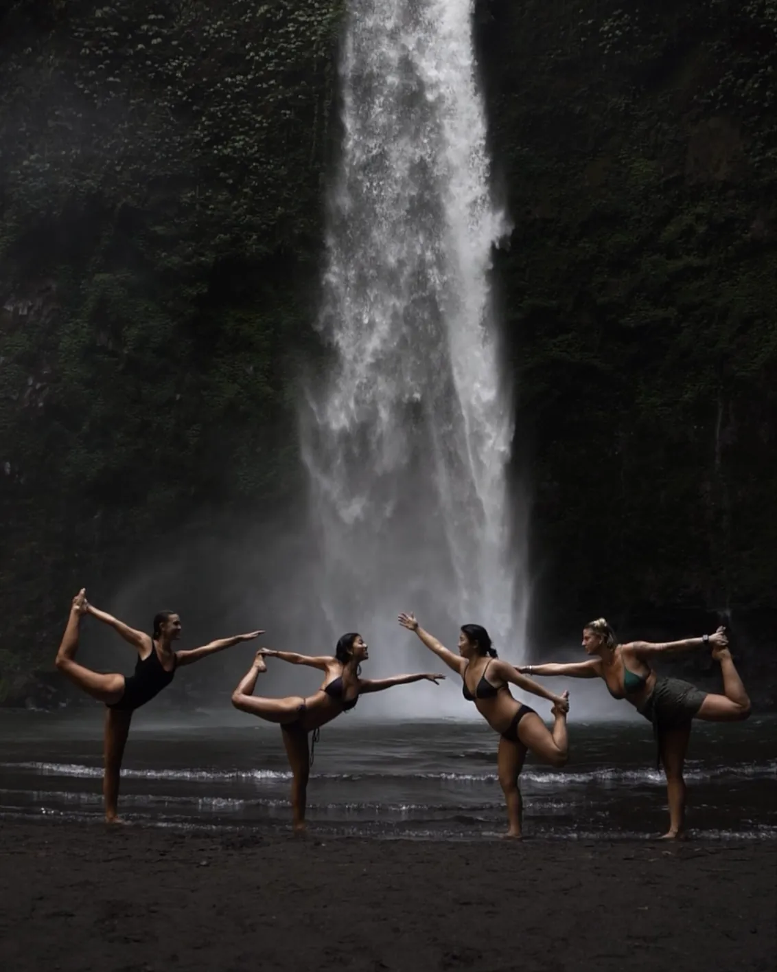 Four women in dancer’s pose at the foot of a waterfall